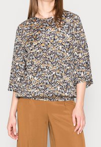 Blusa floreale in navy con motivi gialli, blu e bianchi. Caratterizzata da un colletto rotondo, maniche ¾ e una vestibilità ampia. Il tessuto appare leggero.