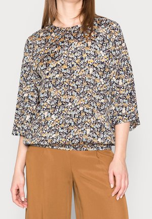Blomstret bluse i marineblå med mønstre i gul, blå og hvid. Har rund halsudskæring, ¾ ærmer og en løs pasform. Stoffet virker let.