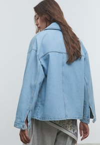 Svetloblažna denim jakna s prostim krojem, ovratnikom in stranskimi razpoki. Ima klasične šivi in zapnete manšete. Gladka tekstura.
