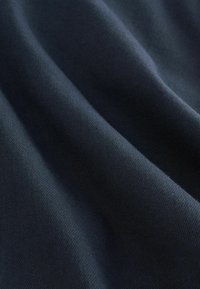 Ciemnonavy materiał o gładkiej, lekko teksturowanej powierzchni, z widocznymi miękkimi fałdami i delikatnymi drapowaniami. Brak widocznych wzorów lub detali metalowych.