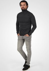 Suéter de cuello alto gris oscuro hecho de tejido de punto, combinado con jeans ajustados gris claro y zapatos negros con una suela en contraste.