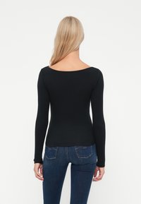 Svart langermet topp med båtutringning, tettsittende design og myk tekstur, kombinert med blå denimjeans som har to baklommer.