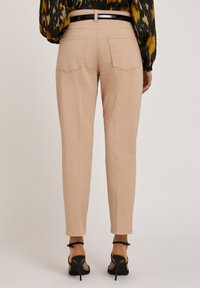 Ljust beige tapered byxor med bakfickor, strukturerad tyg och slät midja. Bärs med svarta sandaletter med hög klack och remmar.