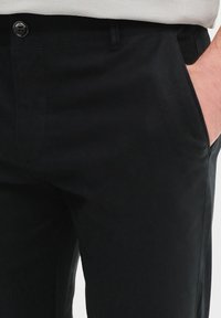 Czarne bawełniane spodnie o gładkiej strukturze, z zapięciem na guzik i bocznymi kieszeniami. Design zawiera prostą nogawkę i minimalne detale.