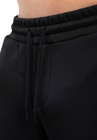 Pantalones de chándal negros con cinturilla elástica, cierre de cordón y bolsillos laterales. Fabricados con un tejido suave y con un diseño ajustado.