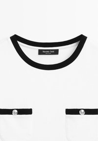 White shirt with black round neckline and two front pockets featuring black trim and silver buttons, labeled Massimo Dutti.