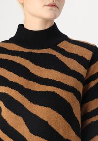 Pull en tricot à rayures marron et noir avec un col haut, doté d'une texture douce et de rayures larges et irrégulières qui créent un motif audacieux.