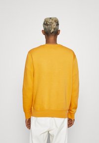 Geel sweatshirt met lange mouwen, ronde hals en geribbelde manchetten; gladde textuur met een casual pasvorm, gedragen over een witte broek.