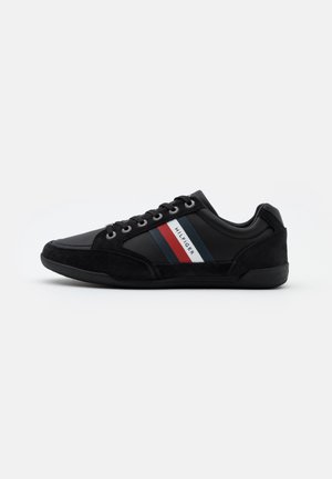 Sort lavtop sneaker med ruskindsdetaljer, snørelukning og rød, hvid og blå stribe branding med teksten "Hilfiger" på siden.