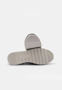 Černá podrážka boty s vzorovanou, strukturovanou šedou gumovou podrážkou; obsahuje drážky a zvýrazněný podpatek. Jednoduchý, funkční design.