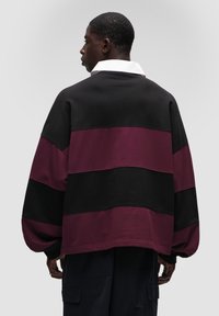 Černý, burgundský a fialový pruhovaný oversized svetřík s bílým límcem, který má žebrované manžety a jemnou texturu.