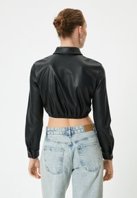 Blouse en cuir noir raccourcie avec de longues manches, un col et une taille élastique, associée à un jean taille haute délavé avec une patch en cuir.