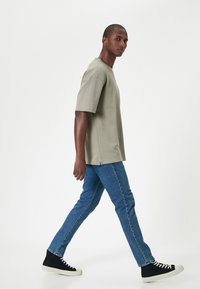Camiseta de manga corta gris claro con un corte relajado, combinada con jeans de mezclilla azul y zapatillas altas negras con suelas blancas.
