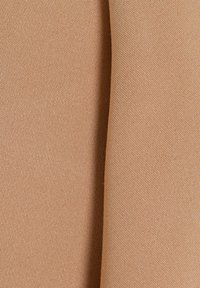 Nærbillede af tæt vævet beige stof, der viser sin tekstur og en tydelig vertikal fold ned ad midten.