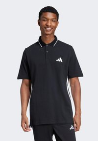 Sort polo skjorte med korte ærmer, hvide krave detaljer og et hvidt logo på brystet. Har et klassisk design og en glat tekstur.