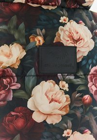 Látka s květinovým vzorem, na které jsou velké pivonky a listy v odstínech krémové, vínové a zelené. Obsahuje černou etiketu s raženým textem.