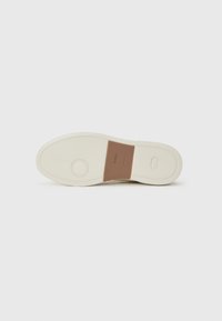Semelle de sneaker blanche avec une surface en caoutchouc texturé, présentant une pièce d'accent marron au centre. Détail de logo circulaire près du talon.
