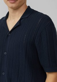 Marineblauwe polo met korte mouwen van gebreid materiaal, voorzien van een textuurpatroon, een kraag en een knoopsluiting. Het materiaal lijkt zacht en ribbelig.
