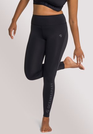 Black leggings with a high waist and logo detail along the leg. Made from a smooth, stretchy material, designed for comfort and movement.