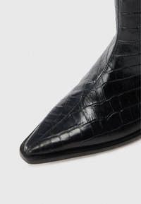 Μαύρο δερμάτινο μποτάκι αστραγάλου με μυτερή μύτη, διαθέτει υφή κροκόδειλου και λεία επιφάνεια. Λεπτή σόλα και κομψός σχεδιασμός.