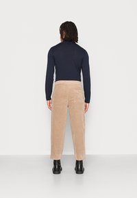 Marineblauwe lange mouwen top gecombineerd met beige corduroy broek. De broek heeft een achterzak en zwarte enkellaarzen maken de outfit af.