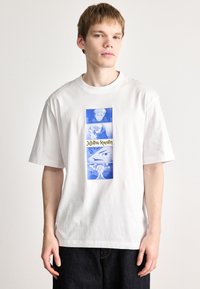 Λευκό βαμβακερό T-shirt με μπλε γραφικό σχέδιο που περιλαμβάνει τέσσερα πάνελ από το "Jujutsu Kaisen" και κίτρινο κείμενο κεντραρισμένο κάτω από τις εικόνες.