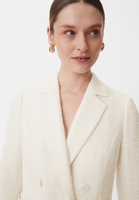 White textured blazer with a double-breasted design, notch lapels, and two buttons. Features subtle fabric pattern and a structured fit.