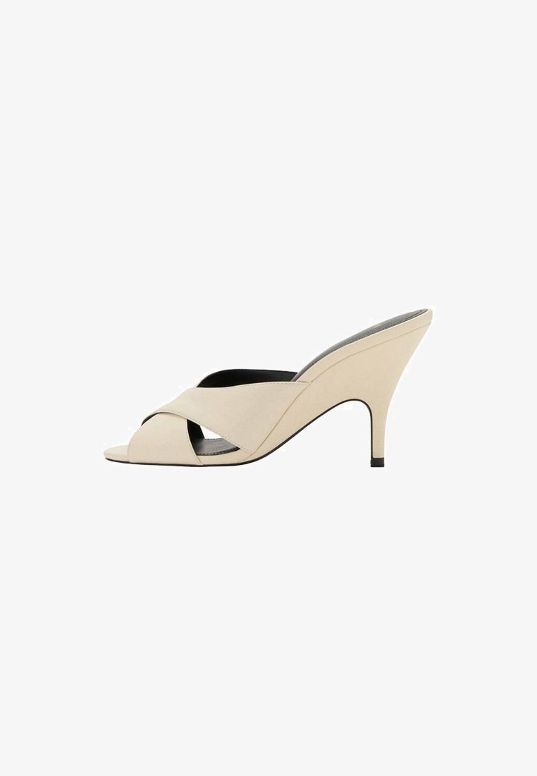 Beige open-toe hakken met kruislings straps en een slanke, taps toelopende hak. Gladde textuur en minimalistisch ontwerp.