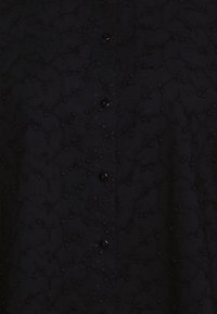 Svart skjorta med en strukturerad mönstring med upphöjda prickar, framknäppning och subtil broderad detaljering genom hela skjortan.
