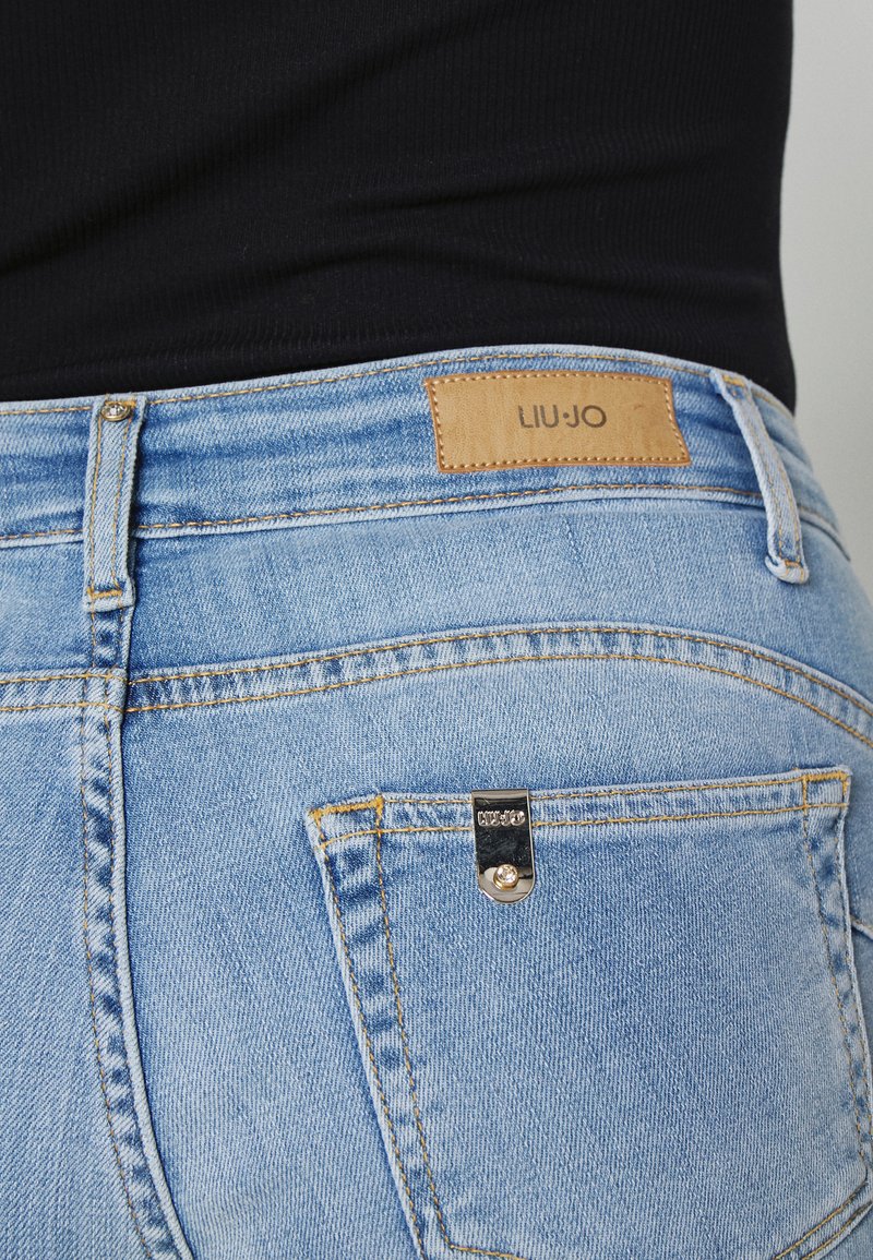 Hellblaue Denim-Jeans mit einem Lederlabel von LIU JO, ausgestattet mit einem Knopfverschluss, sichtbaren Nähten und einer kleinen dekorativen Taschenakzentuierung.