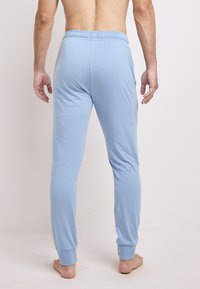 Lichtblauwe, strakke pyjamabroek met een elastische tailleband en opgerolde enkels, gemaakt van zacht, rekbaar materiaal, getoond vanuit de achterkant.