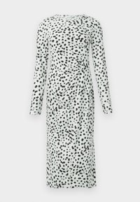 Robe à manches longues présentant une base vert clair avec des motifs à pois noirs. Le tissu est plissé d'un côté, créant de la texture et un intérêt visuel.