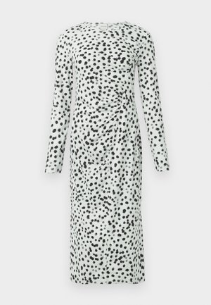 Langärmliges Kleid mit einem hellgrünen Grundton und schwarzen Punkten. Der Stoff ist auf einer Seite gerafft, was Textur und visuelles Interesse erzeugt.