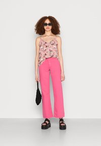 Camisola de alças com estampa floral em bege, combinada com calças largas de cintura alta em rosa-choque. Sandálias de plataforma pretas e uma bolsa preta texturizada.