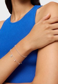 Braccialetti in argento con perline e charm indossati su un braccio nudo, abbinati a un top senza maniche blu a costine.