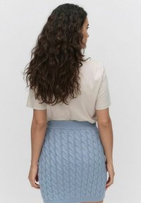 Lyhythihainen beige paita yhdistettynä vaaleansiniseen kaapelikudottuun mini-hameeseen, jossa on ribbineulevyötärö ja teksturoitu kuvio.