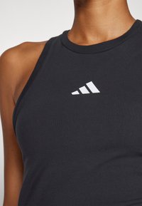 Černý atletický t�ílko s kulatým výstřihem a bez rukávů. Na hrudi je bílý logo Adidas se třemi diagonálními pruhy.