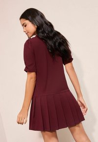 Rochie plisată burgundă cu mâneci scurte bufante și corset strâmt, realizată din țesătură moale, cu textură netedă și design simplu.