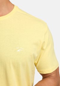 T-shirt en coton jaune avec un col rond et des manches courtes. Présente un logo blanc et le texte "EST. 1993" sur la zone de la poitrine gauche.