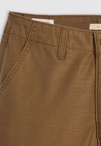 Braune Stoffhose mit strukturiertem Finish, diagonalen Fronttaschen, einem Knopfverschluss und Gürtelschlaufen an der Taille.