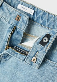 Jeans in denim blu chiaro con zip e chiusura a bottone. Presentano cuciture arancioni e un'etichetta in stoffa all'interno della vita.