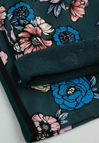 Ciemnozielony materiał z dużymi kwiatowymi wzorami w odcieniach niebieskiego, różowego i koralowego, posiadający złożony mankiet z teksturowanym wnętrzem.