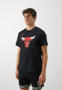 Black cotton t-shirt featuring a red Chicago Bulls graphic on the front, round neckline, and short sleeves, paired with black shorts.