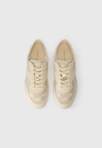 Beige sneakers med overdækning af canvas, der viser et subtilt MK-mønster og tonede snørebånd. Har et guldakcent i snørebåndsområdet for at tilføje detaljer.