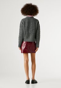 Pelēks, adīts džemperis ar kabelīšu adījumu piedurkņām, kombinēts ar bordo krāsas, spīdīgu mini svārku. Modeli rotā melni loafers.