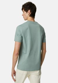 T-shirt in cotone verde con collo rotondo classico, maniche corte e orlo dritto. Tessuto liscio e dettaglio di branding minimale nella parte inferiore.