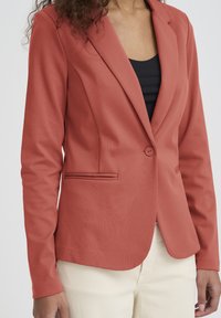 Blazer corail avec une fermeture à un seul bouton, des revers crantés et des poches latérales. Confectionné dans un matériau lisse, design ajusté et manches longues.