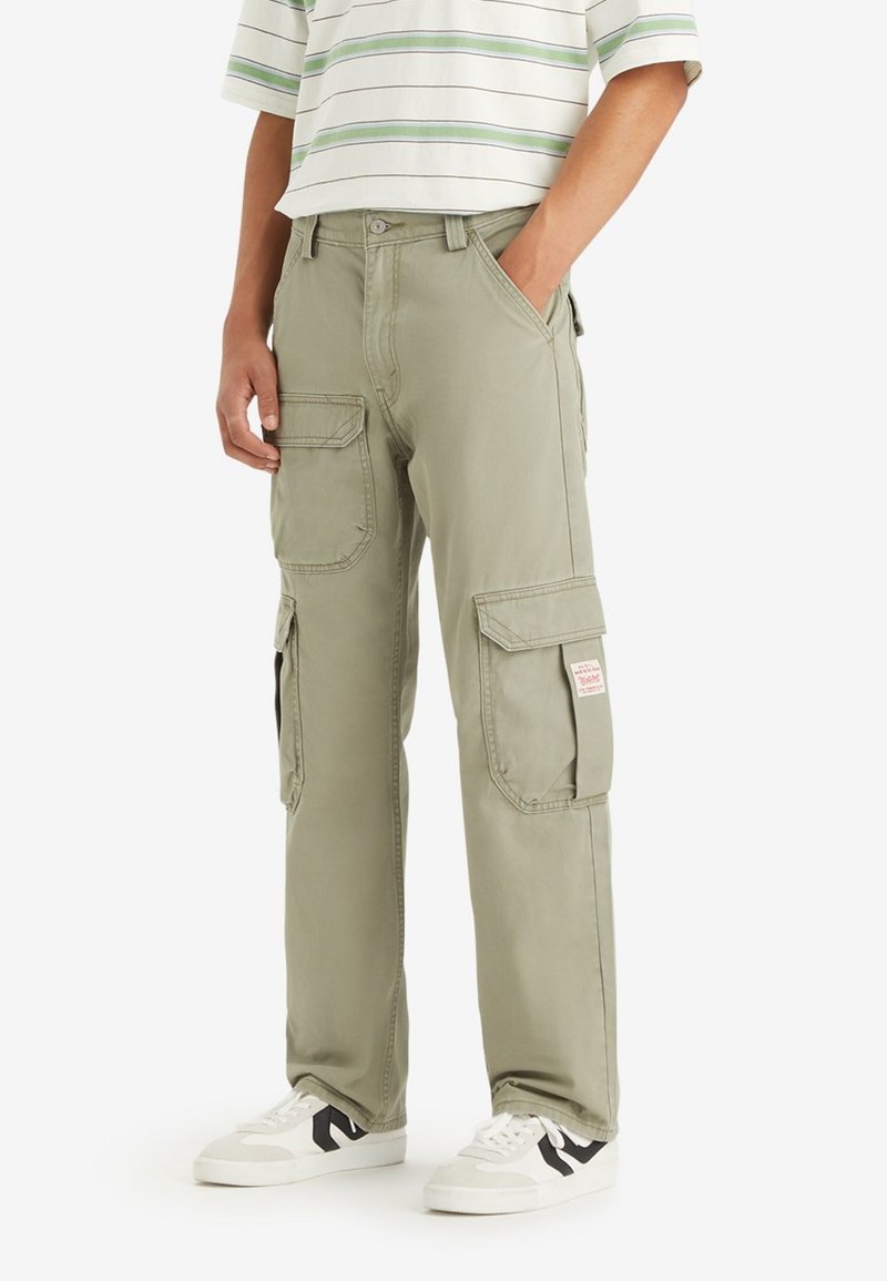 Zelene cargo hlače iz bombaža, ki so opremljene z več stranskimi žepi, sproščenim krojem in blagovno oznako na desnem stegnu.