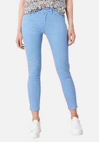 Vaqueros skinny de color azul claro hechos de una mezcla de algodón elástico, con cierre de cremallera, cinco bolsillos y dobladillo hasta el tobillo. Combinados con zapatillas blancas.