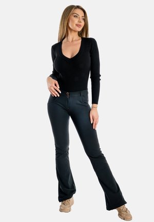 Top lungo a maniche lunghe nero a coste con scollo a V; abbinato a pantaloni neri a campana aderenti con due bottoni decorativi in vita.